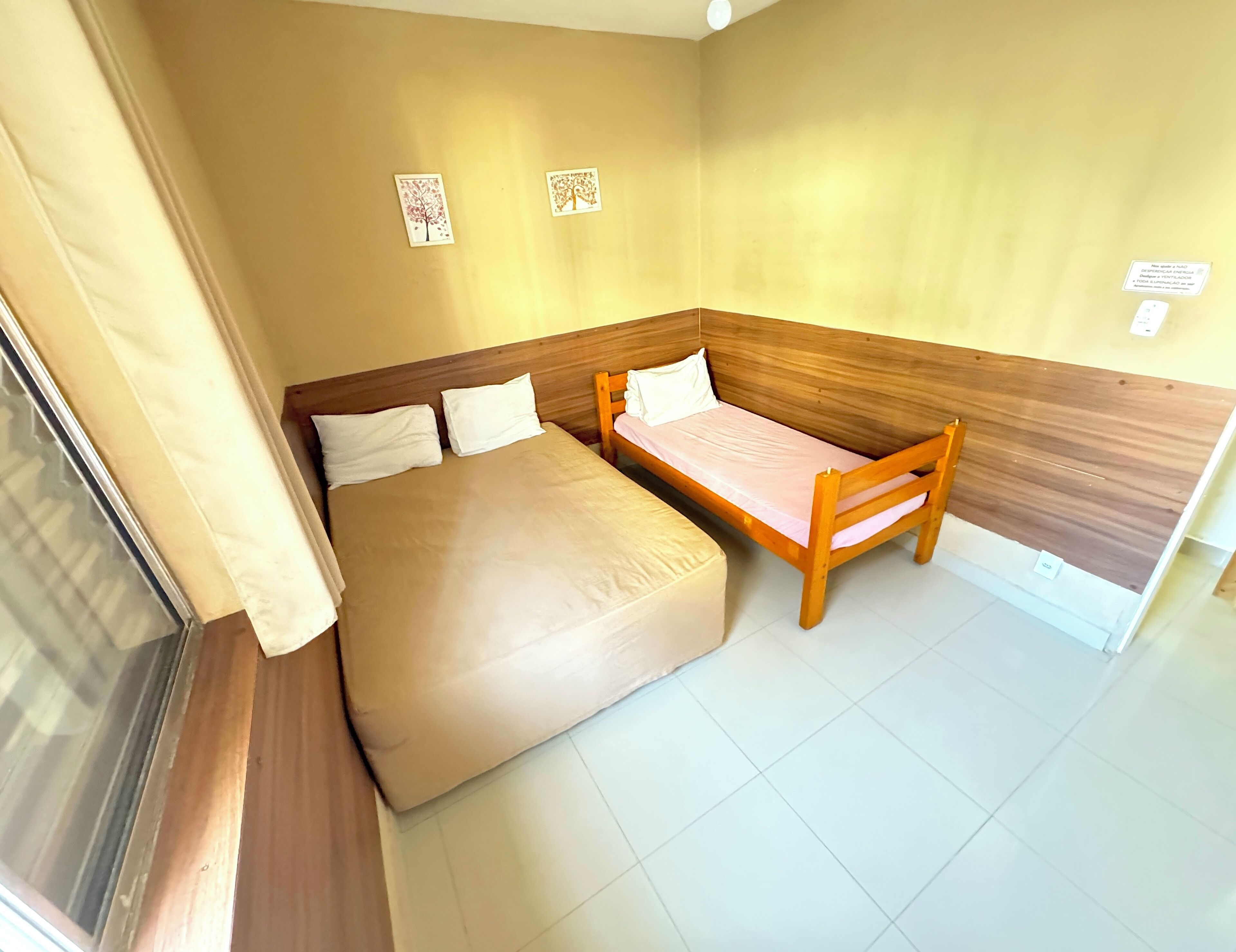 Quarto com uma cama, um banco de madeira e duas imagens penduradas na parede.