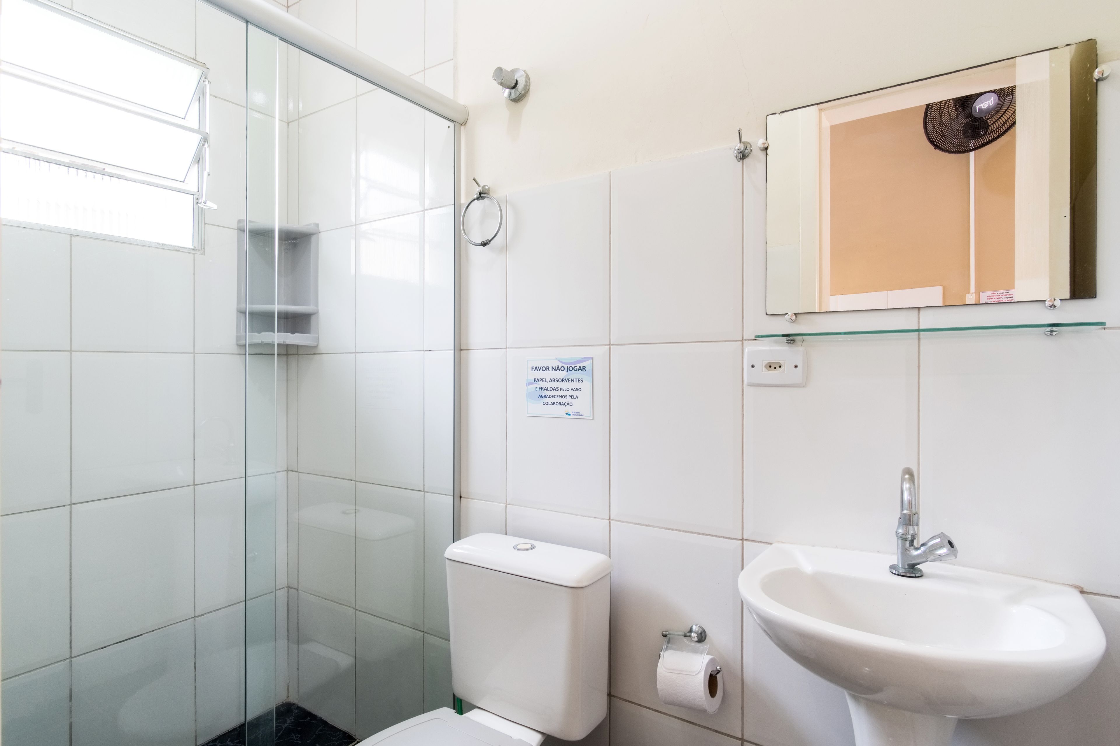 A bathroom with a glass shower enclosure, a toilet, a sink, and a mirror with a fan above it.