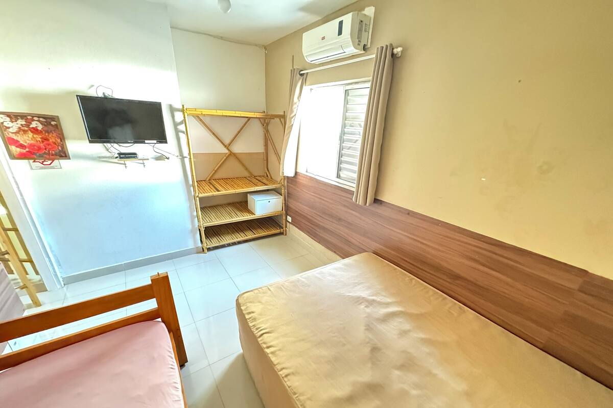 A room with two beds, a TV, a shelf unit, and a window with curtains.