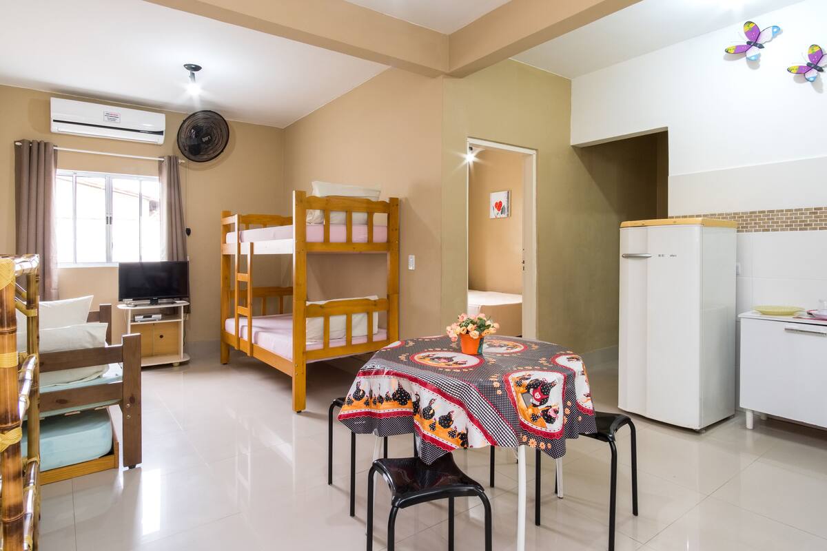 A room with bunk beds, a dining table with a tablecloth, a TV, and a refrigerator.