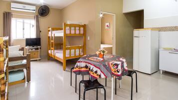 Um quarto com beliches, uma mesa de jantar com toalha e uma televisão, além de uma geladeira.