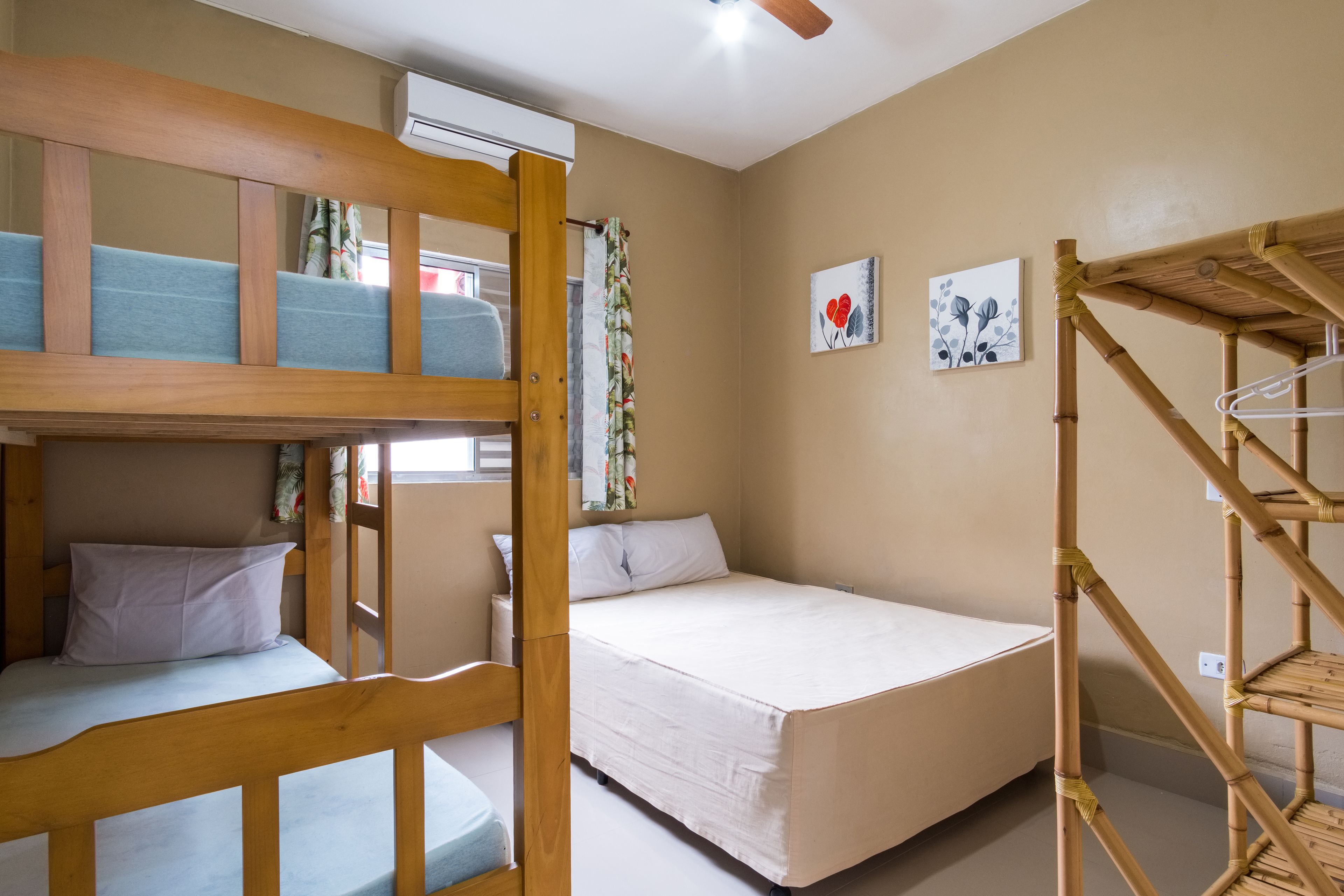 Quarto de dormitório com beliches, uma cama individual, escada de madeira e ar condicionado fixado na parede.