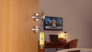 A hotel room with a bed, a desk with a laptop, a television, and a door with a keycard lock. - Hotel & Restaurant Engel (Herbertingen)
