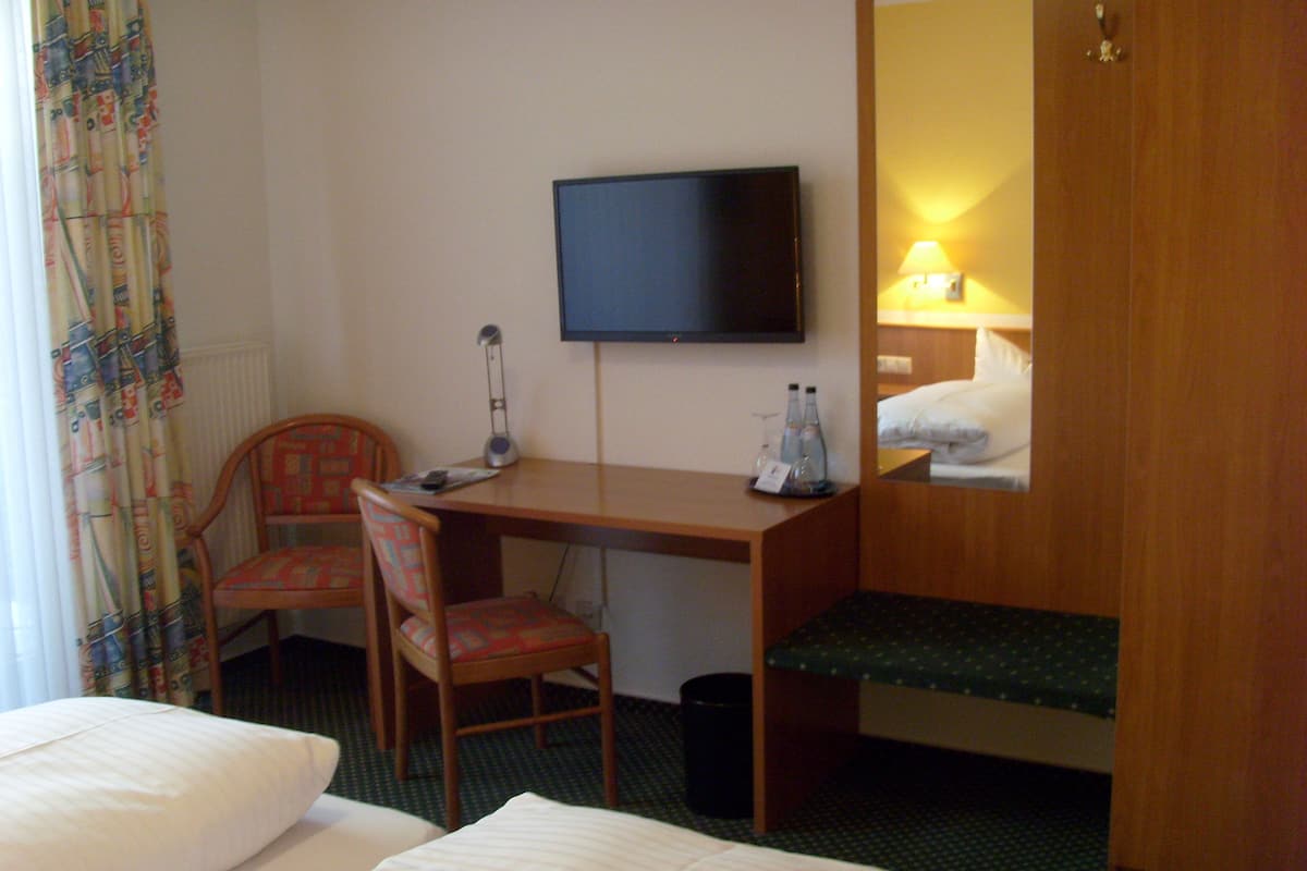Ett hotellrum med en säng, ett skrivbord med en stol, en tv och ett litet bord med flaskor och glas.