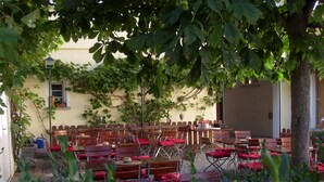 An outdoor seating area with multiple wooden tables and chairs, surrounded by greenery and a building in the background. - Hotel & Restaurant Engel (Herbertingen)