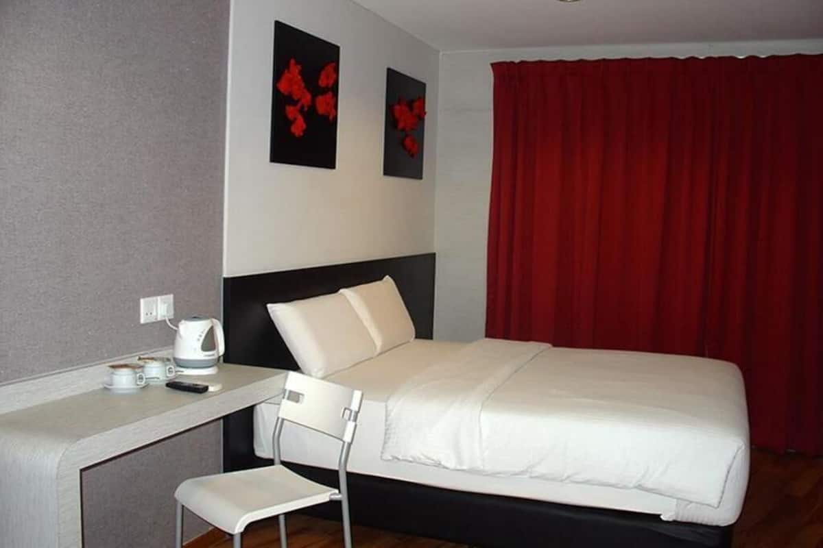 A hotel room with a bed, a desk, a chair, a red curtain, and two wall-mounted artworks.
