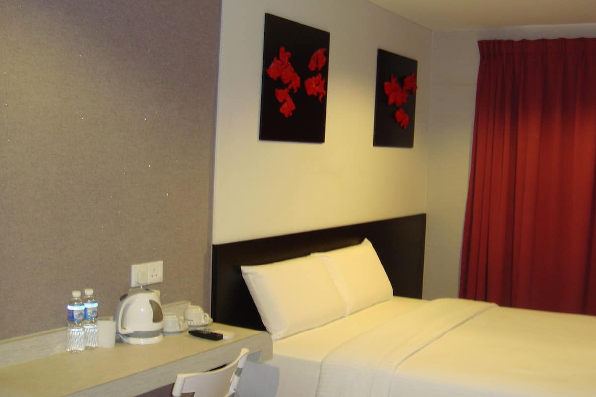 A hotel room with a bed, a bedside table with a mirror, a red curtain, and two wall-mounted flower decorations.