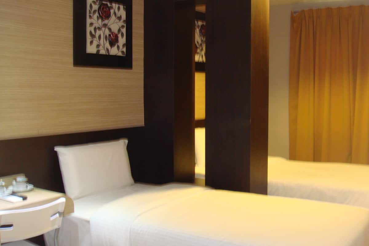 A hotel room with two beds, a bedside table with a lamp, and a wall-mounted artwork.