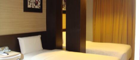 A hotel room with two beds, a bedside table with a lamp, and a wall-mounted artwork.