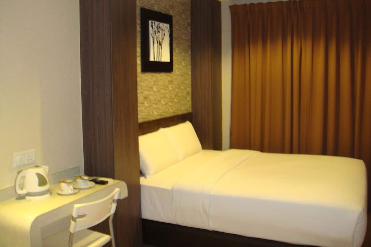A hotel room with a bed, a desk with a chair, a coffee maker, and a framed picture on the wall.