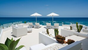 A rooftop terrace with white lounge chairs and umbrellas, overlooking a clear blue sea. - Lani's Suites de Luxe  (Tias)
