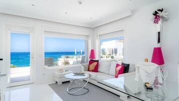 A modern living room with a glass coffee table, white sofa with colorful cushions, and a view of the ocean.