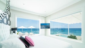 A hotel room with a large bed, a view of the ocean, and a balcony with lounge chairs. - Lani's Suites de Luxe  (Tias)