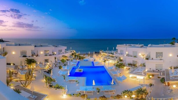 A resort with a central swimming pool, multiple lounge areas, and a view of the sea. - Lani's Suites de Luxe  (Tias)