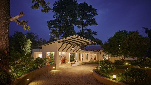 A modern building with a covered entrance, surrounded by trees and a landscaped garden. - Club Mahindra Kanha (Bichhiya)
