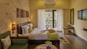 A hotel room with a bed, a sofa, a small table, a TV, and a balcony with a view. - Club Mahindra Kanha (Bichhiya)