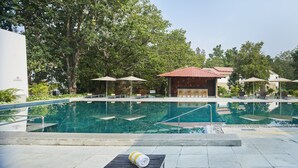 A swimming pool with lounge chairs and umbrellas, surrounded by trees and buildings. - Club Mahindra Kanha (Bichhiya)
