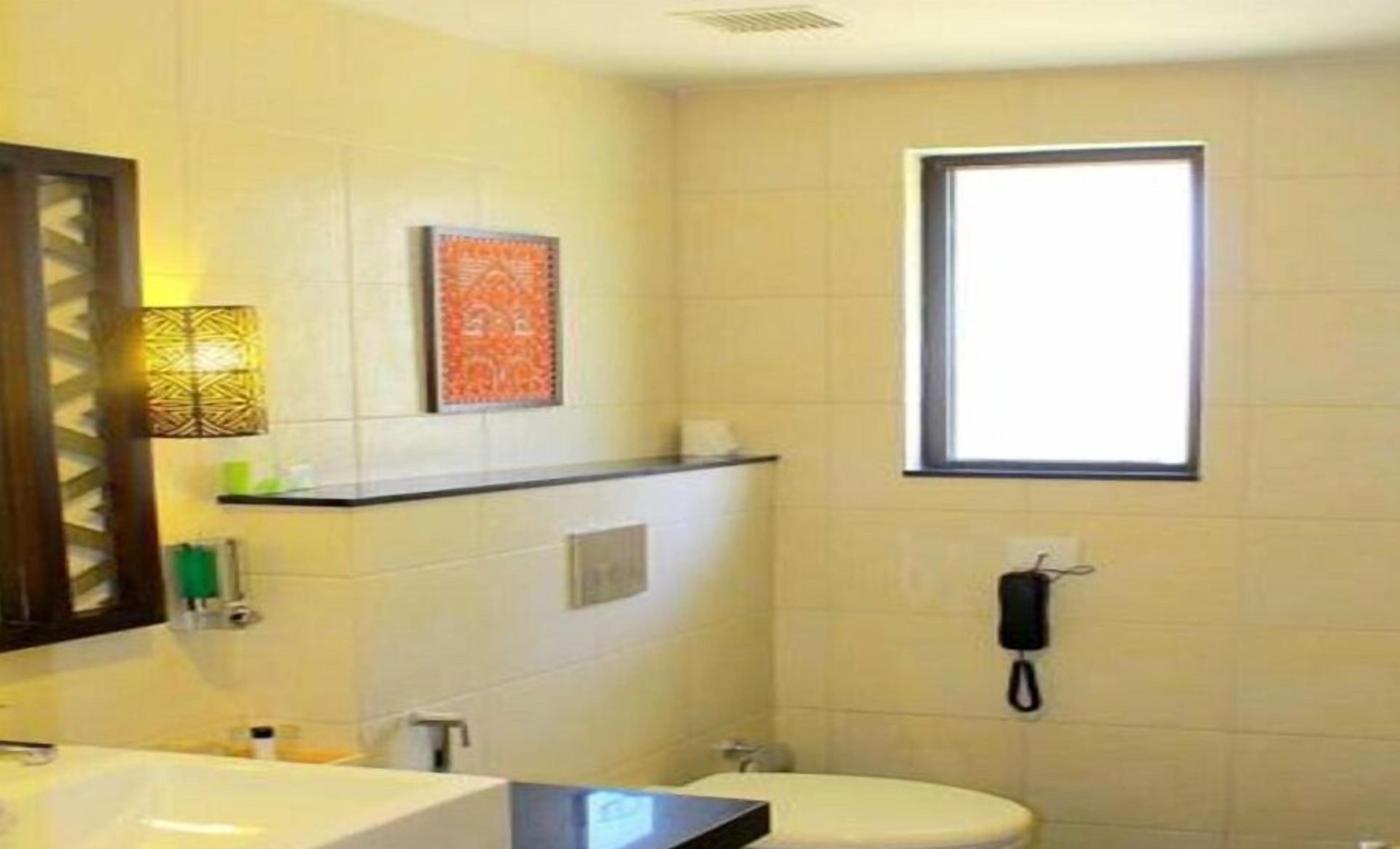 Un baño con lavamanos blanco, espejo, inodoro y ventana.