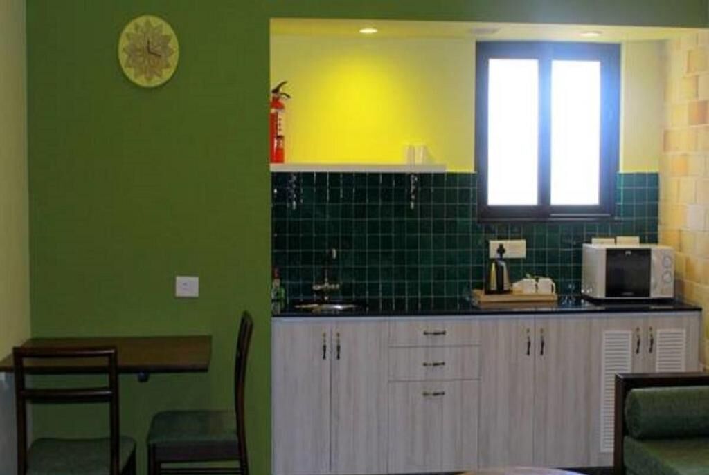A compact kitchen with a green wall, a clock, and a window.