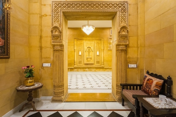 Un pasillo con puertas doradas ornamentadas, un candelabro, un suelo estampado y una cama con almohada decorada.