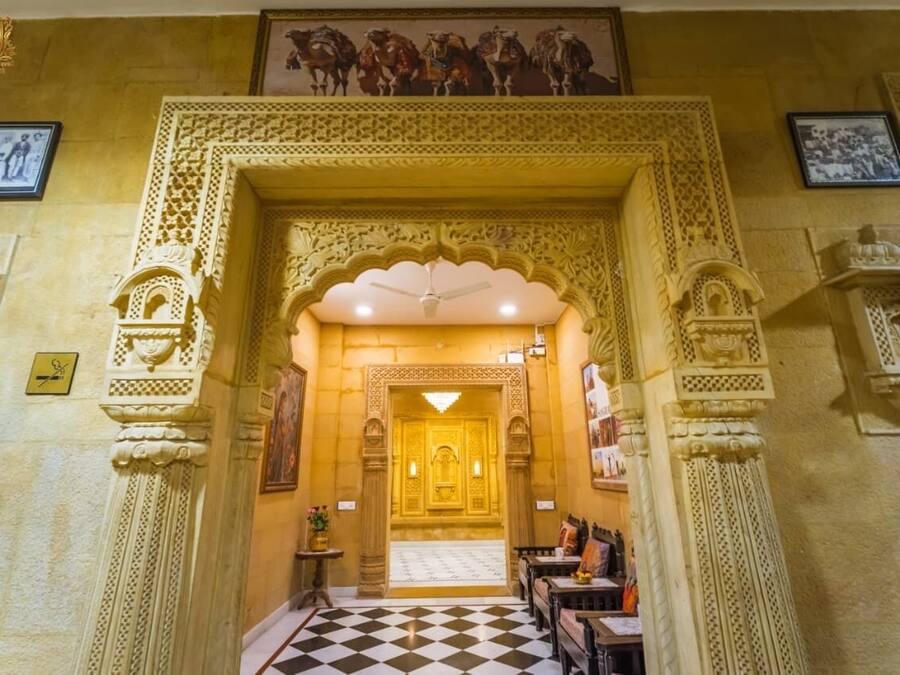 An ornate entrance with intricate carvings, a checkered floor, and framed pictures on the walls.
