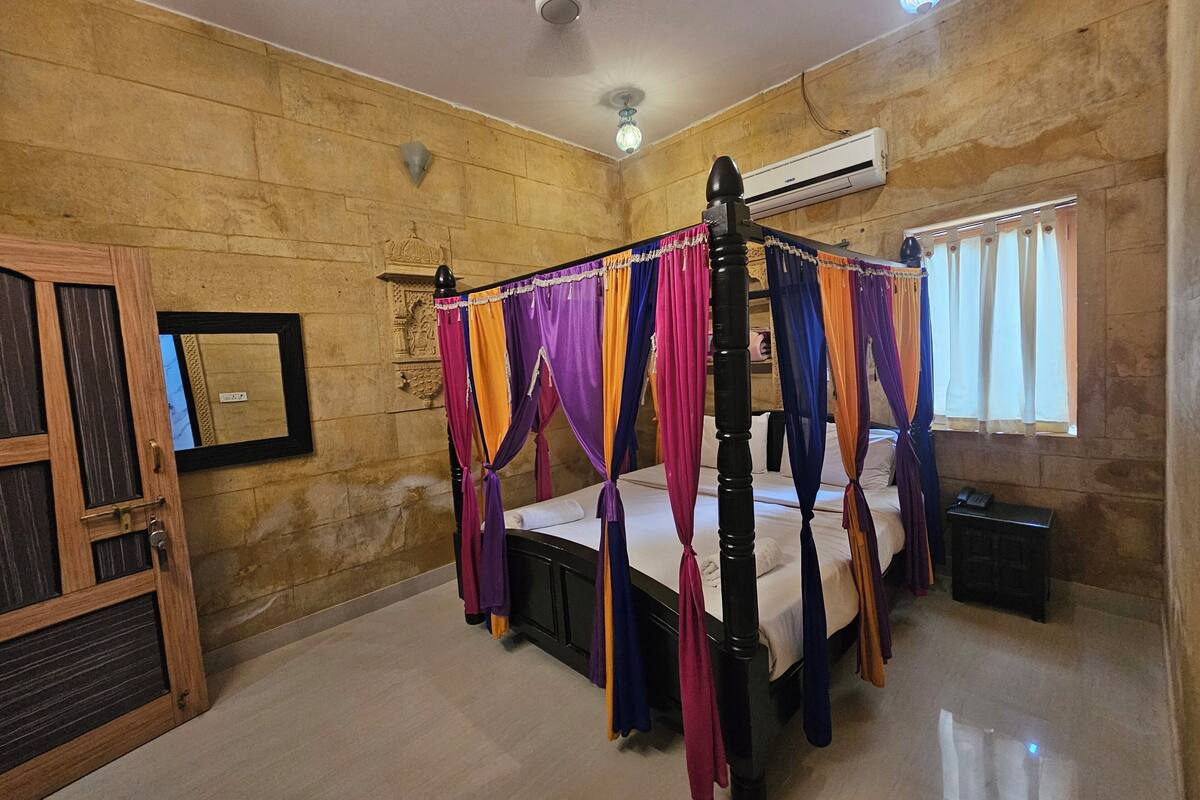Une chambre dotée d’un lit à baldaquin, d’une porte en bois, d’un climatiseur mural et d’une fenêtre avec des rideaux.