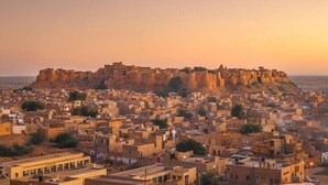Un paisaje urbano histórico con una fortaleza destacada en una colina que domina una zona urbana densamente poblada.