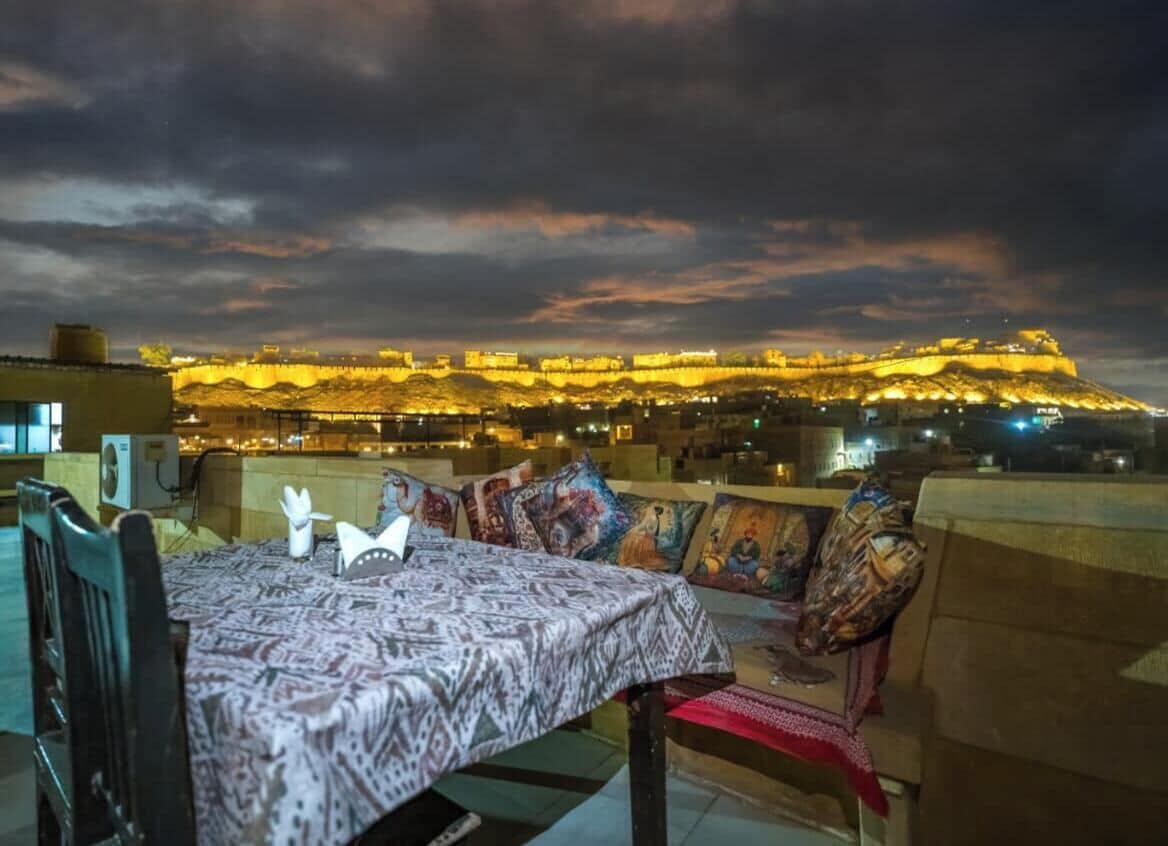 A dining area with a table set for two, overlooking a historic fortress illuminated at night.