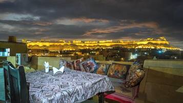 A dining area with a table set for two, overlooking a historic fortress illuminated at night.