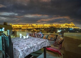 Un comedor con una mesa dispuesta para dos personas, con vista a una fortaleza histórica iluminada por la noche.