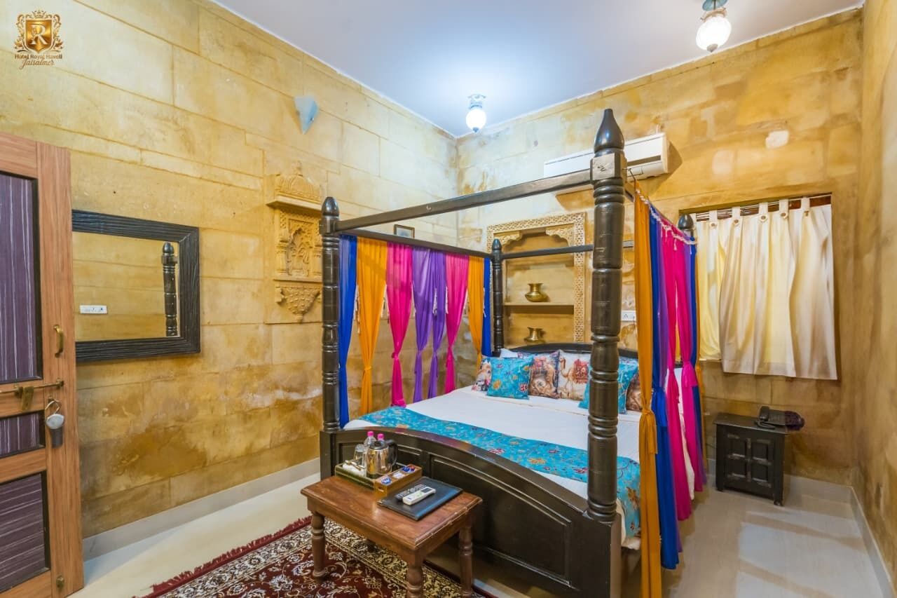 A four-poster bed with colorful drapes, a bedside table with a remote control, and a small cabinet.
