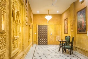 Um corredor com esculturas elaboradas nas paredes, um candelabro e uma porta com desenhos complexos.