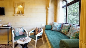 Une pièce comprenant un canapé, des fauteuils, une petite table, un miroir et une fenêtre donnant sur des arbres.