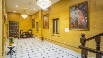 Un couloir avec un sol à motifs, un lustre, un escalier et un tableau accroché au mur.