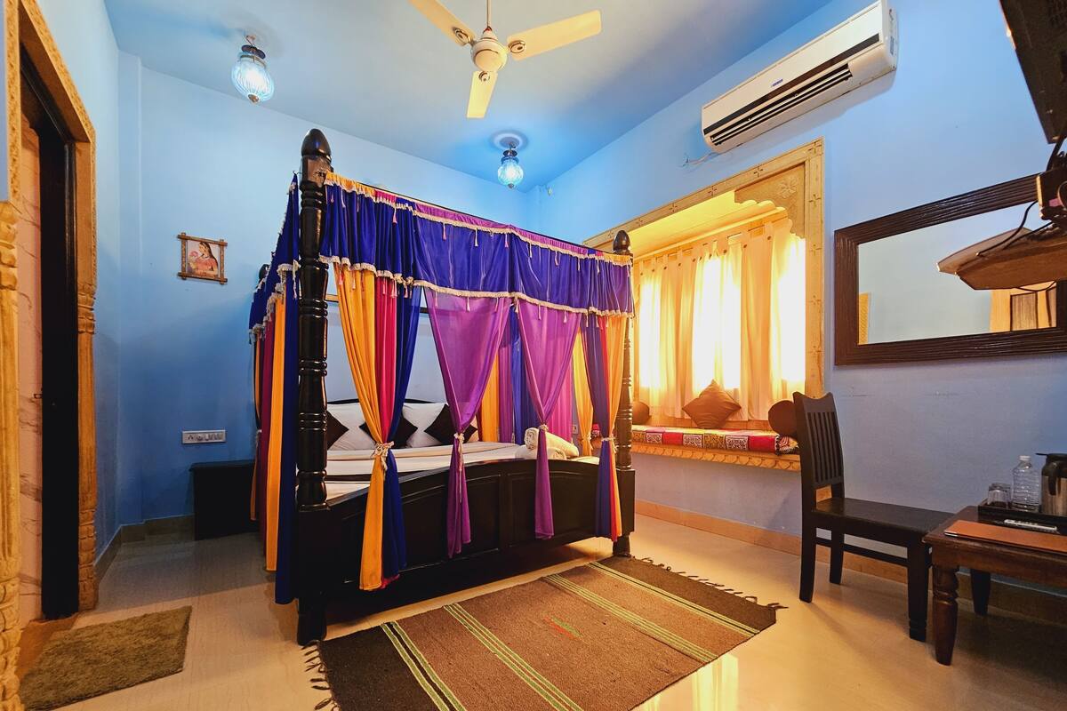 Une chambre à coucher avec un lit à baldaquin, un ventilateur de plafond, un appareil de climatisation, une fenêtre avec des rideaux, une table de chevet et une chaise.