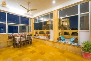 Una habitación con una mesa de comedor y sillas, un banco con cojines, ventanas amplias y un ventilador de techo.