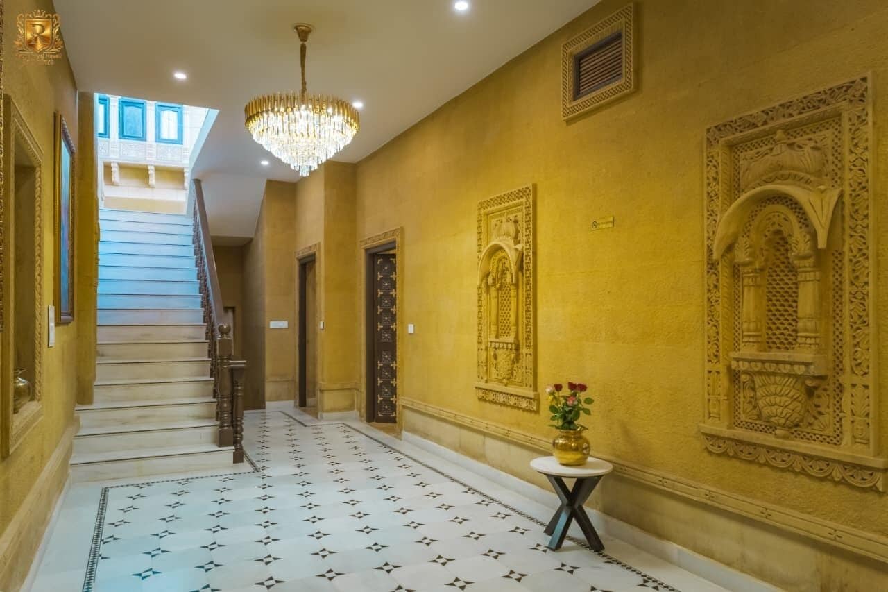 Um corredor com escada, um candelabro e detalhes decorativos nas paredes.