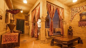 A traditional room with a wooden table, a bench, and a patterned rug. - Hotel Garh Jaisal Haveli (Jaisalmer)