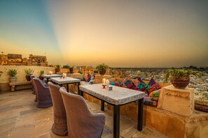 A rooftop terrace with stone flooring, tables, chairs, and potted plants. - Hotel Garh Jaisal Haveli (Jaisalmer)