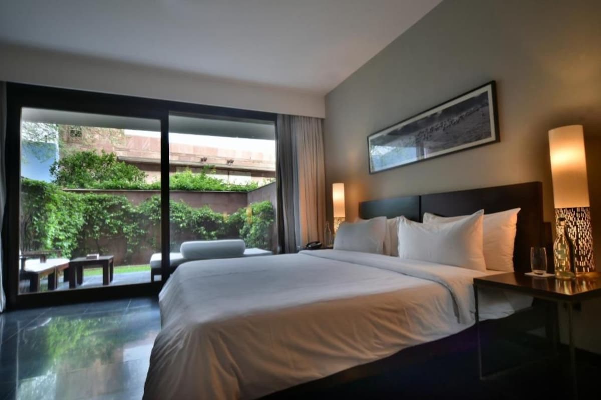 Habitación de hotel con una cama grande, un escritorio y vista a un jardín a través de una puerta corrediza.