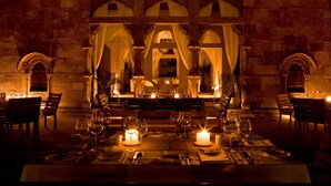 A dimly lit dining area with candlelit tables, stone walls, and arched windows. - RAAS Jodhpur (Jodhpur)