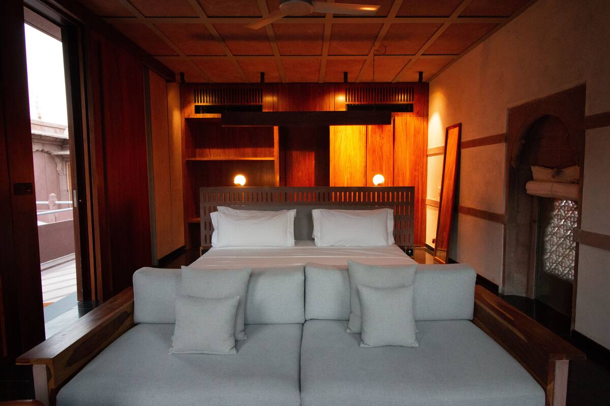 A modern hotel room with a large bed, a sofa, and a view of the outside.