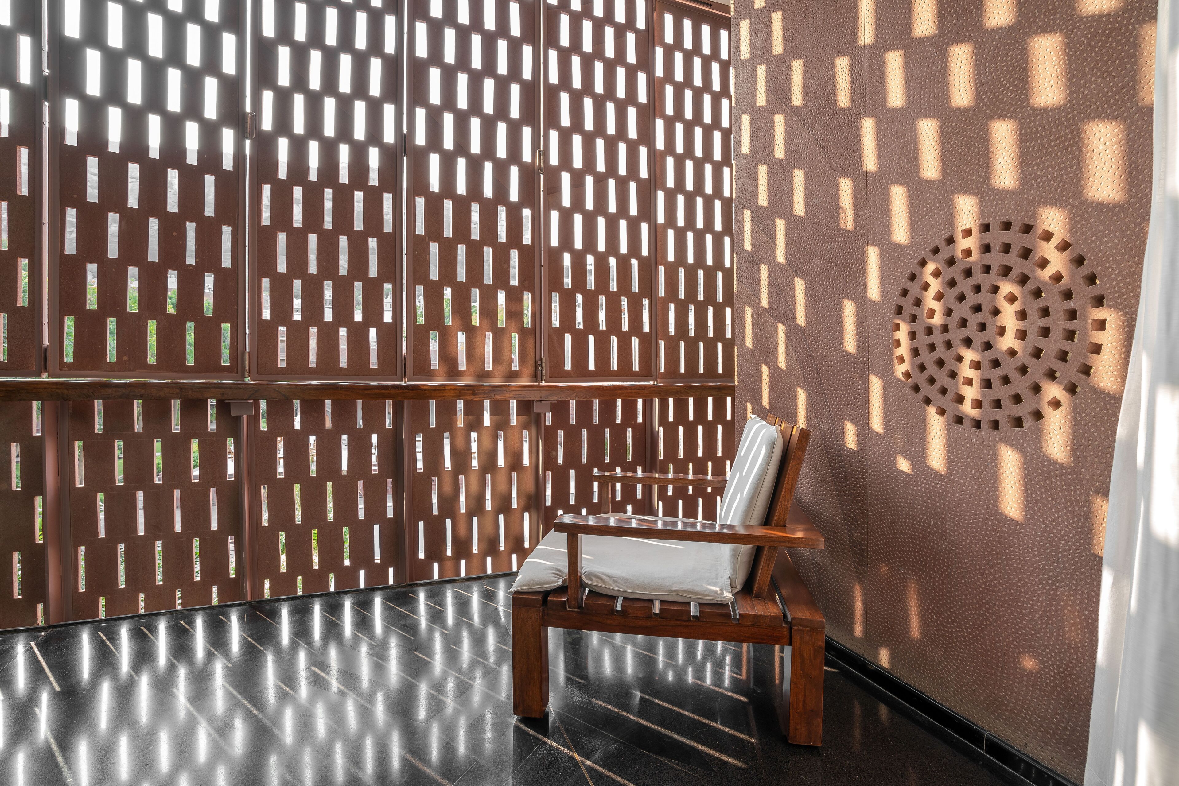 A wooden chair with a cushion, a patterned wall, and a circular ventilation feature.