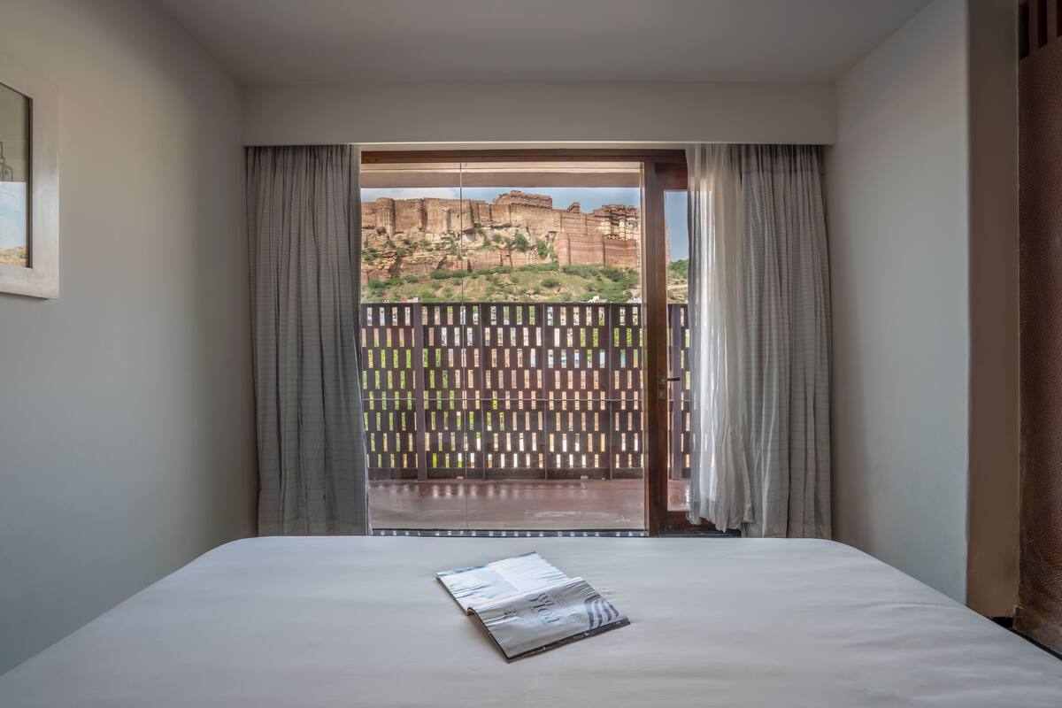 A hotel room with a bed, a window with curtains, and a view of a rocky landscape.