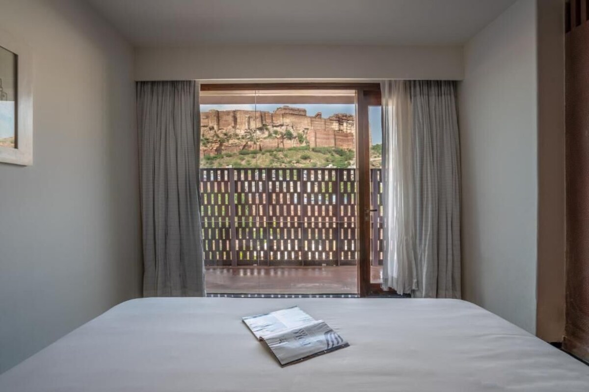 A hotel room with a bed, a window with curtains, and a view of a mountainous landscape.