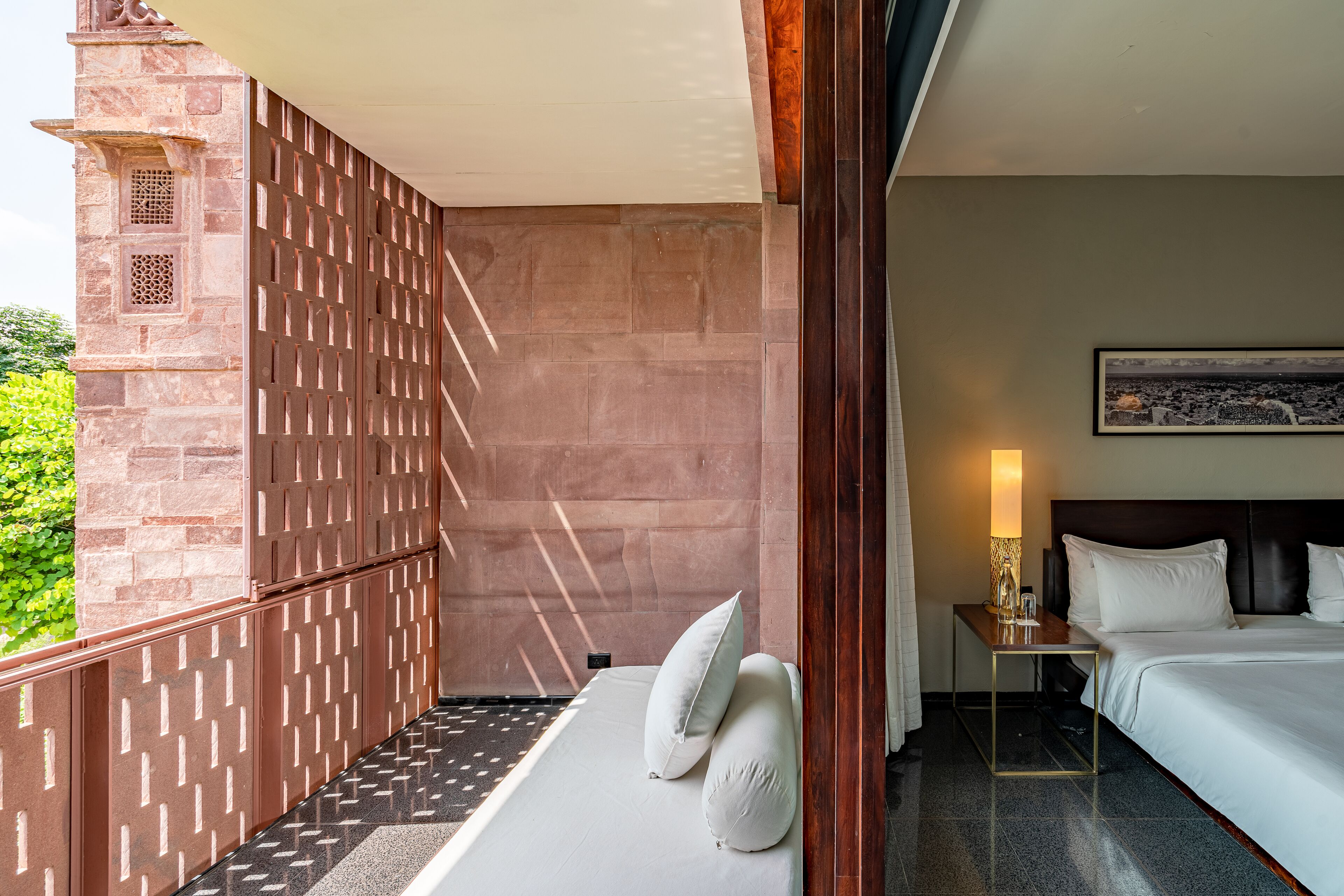 A hotel room with a bed, a nightstand, and a view of a cityscape.
