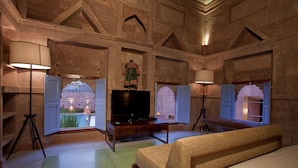 A spacious room with a large bed, a television, and a sofa. There are windows with views of greenery and a building. - RAAS Jodhpur (Jodhpur)