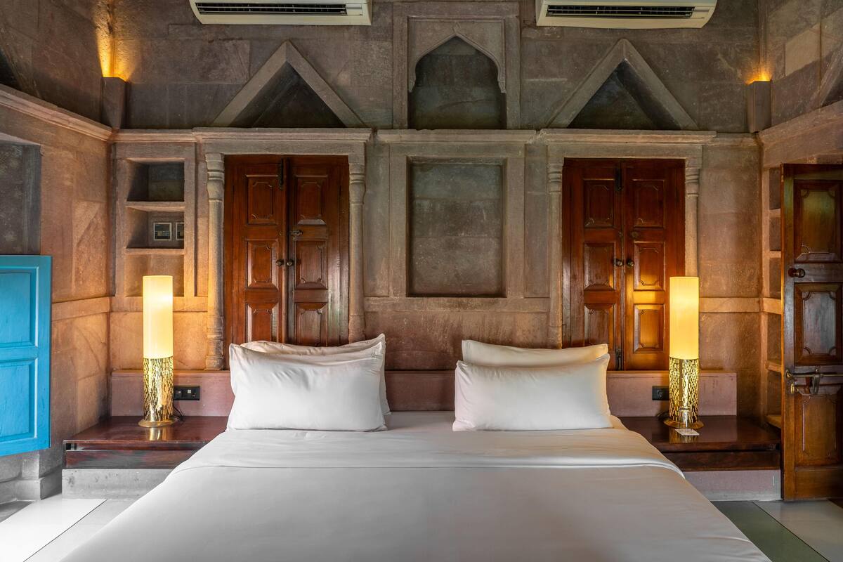 A double bed with two nightstands, each with a lamp, in a room with stone walls and wooden doors.