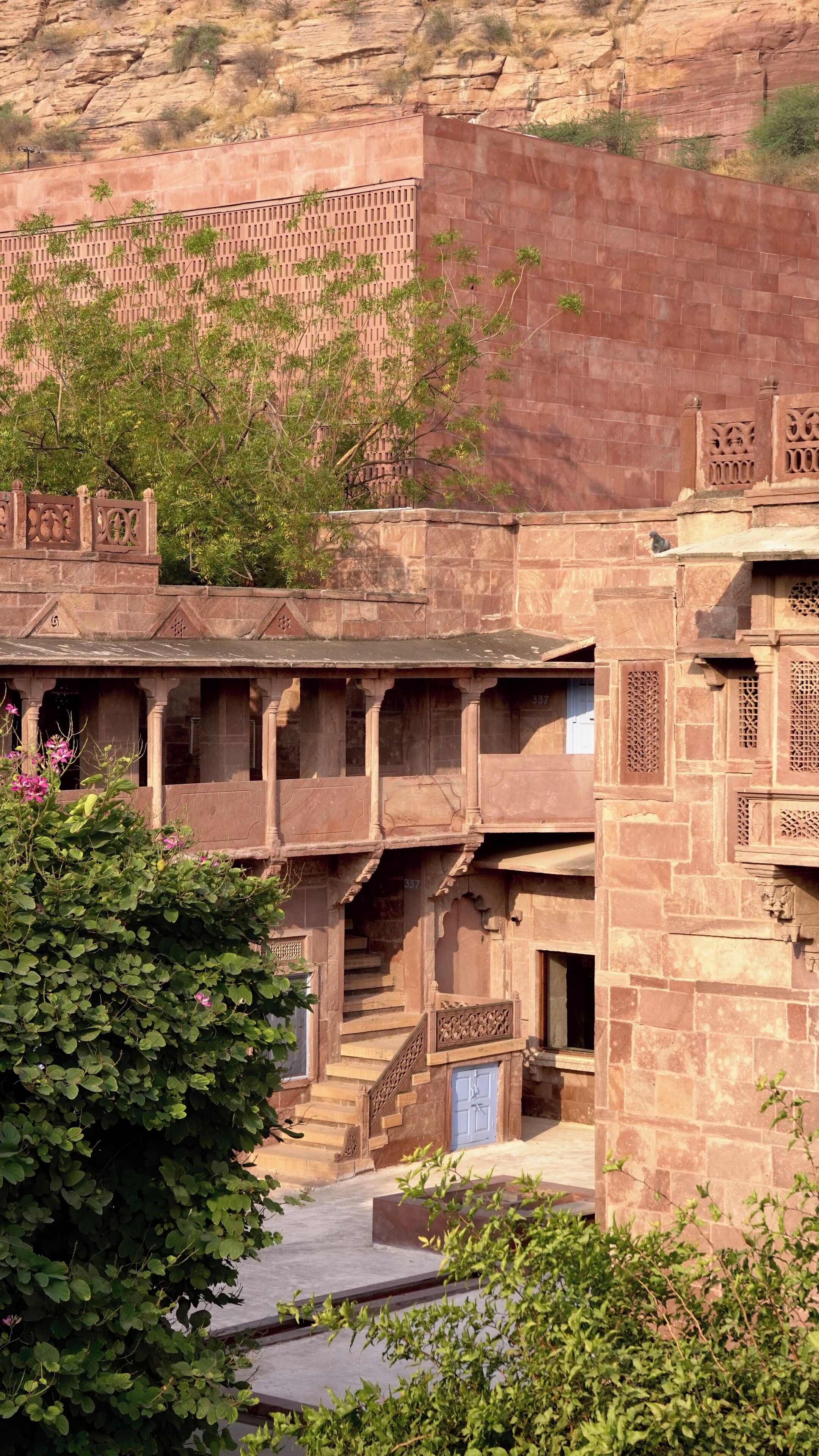 Un edificio tradicional con fachada de piedra, una escalera que lleva a un nivel superior y un pequeño jardín al frente.