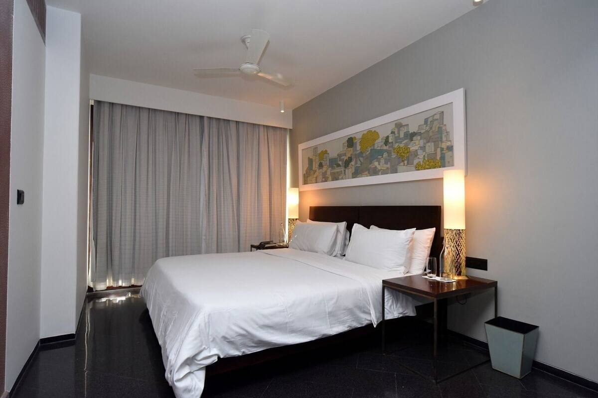 A hotel room with a large bed, a nightstand, a lamp, a ceiling fan, and a painting on the wall.